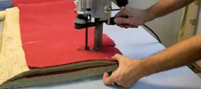 A man using a machine to cut a piece of fabric.