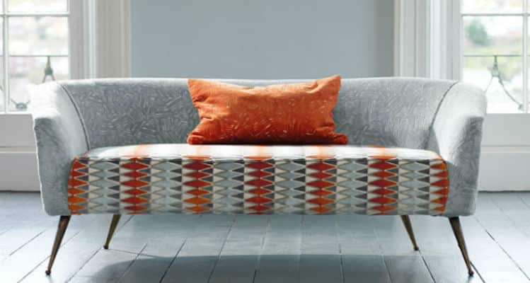 A grey sofa with orange pillows in a room.