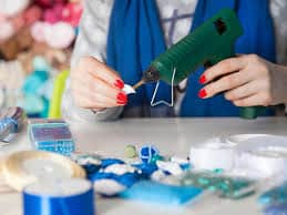 A woman is using a glue gun on a table.