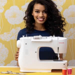 A young woman with a sewing machine in front of a yellow wall.