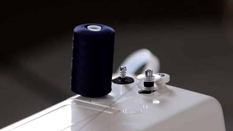 A sewing machine with a blue spool of thread that utilizes a bobbin.