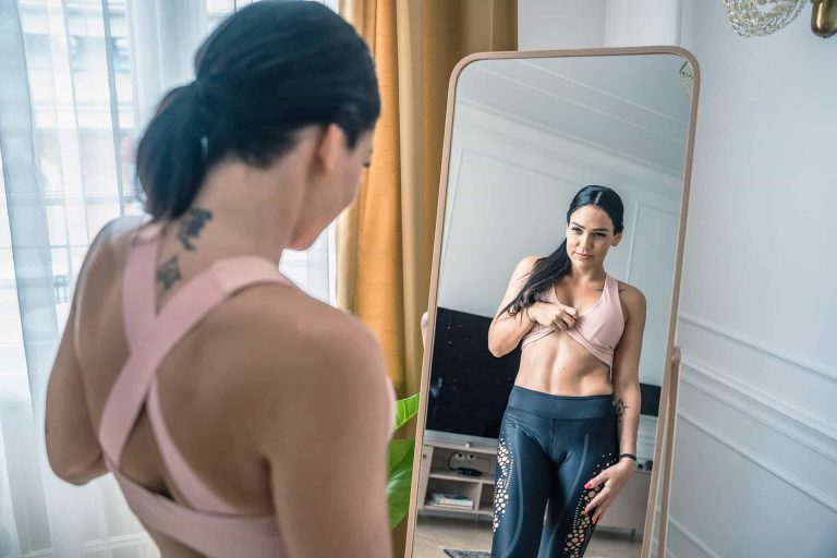 A woman in a sports bra looking at herself in the mirror.